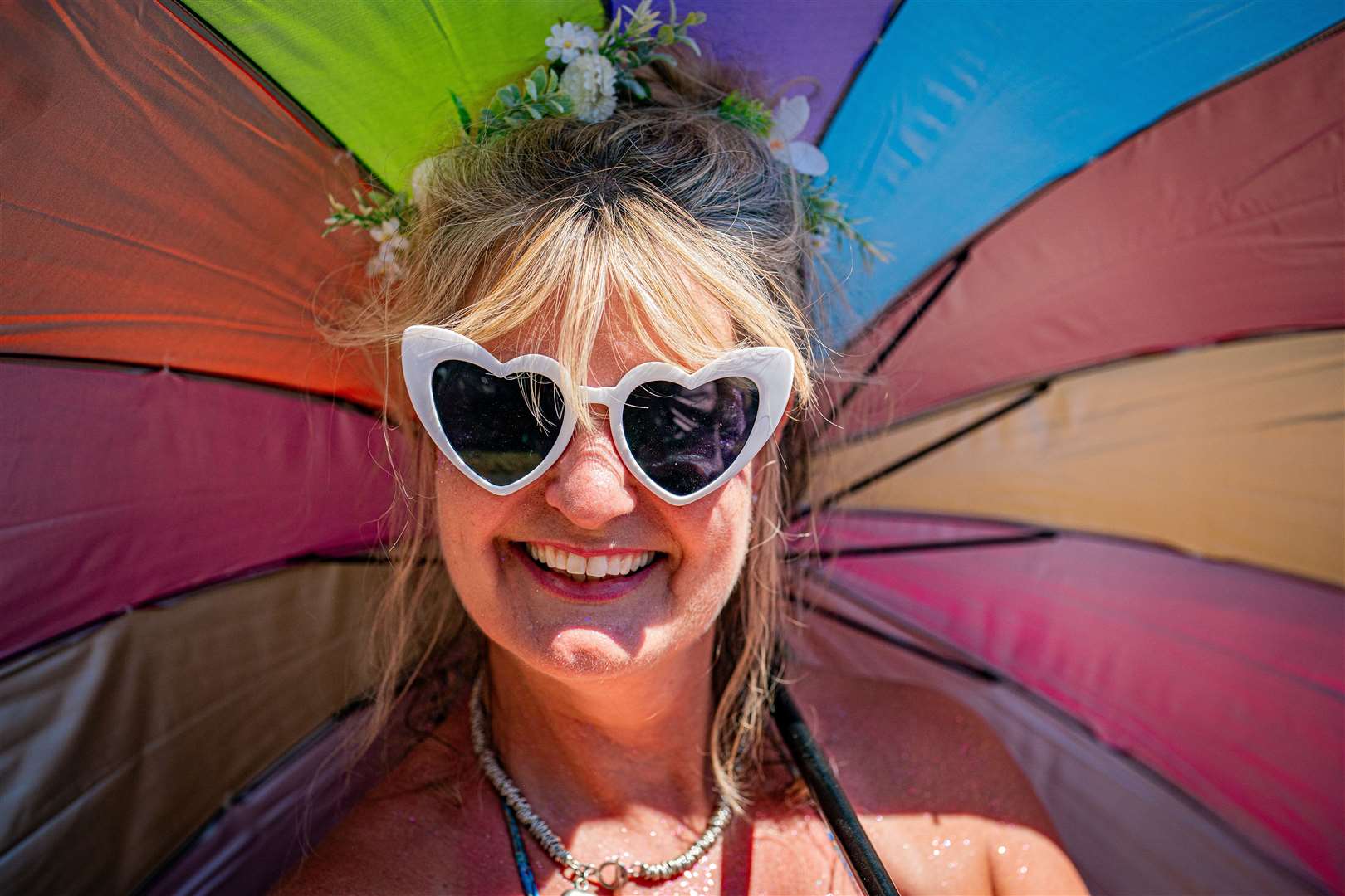 A festivalgoer wears heart-shaped sunglasses and carries a colourful brolly (Ben Birchall/PA)
