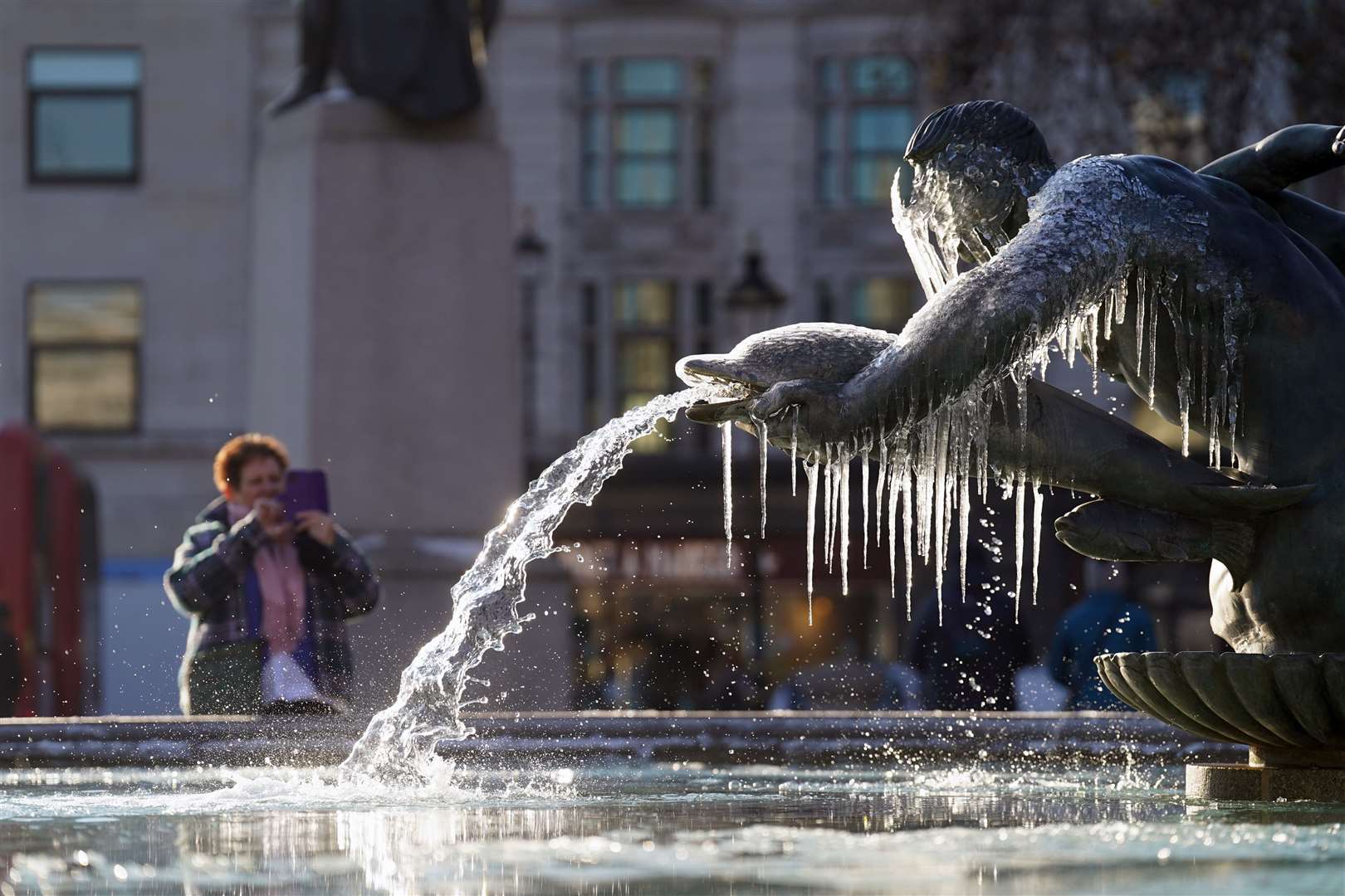 A person takes a picture of a frozen fountain in Trafalgar Square, central London (Stefan Rousseau/PA)