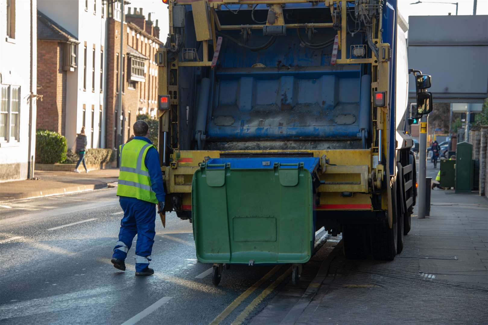 bin lorry or waster truck collects refuse from a green dumpster with council bin worker operating mechanism in a yellow vest