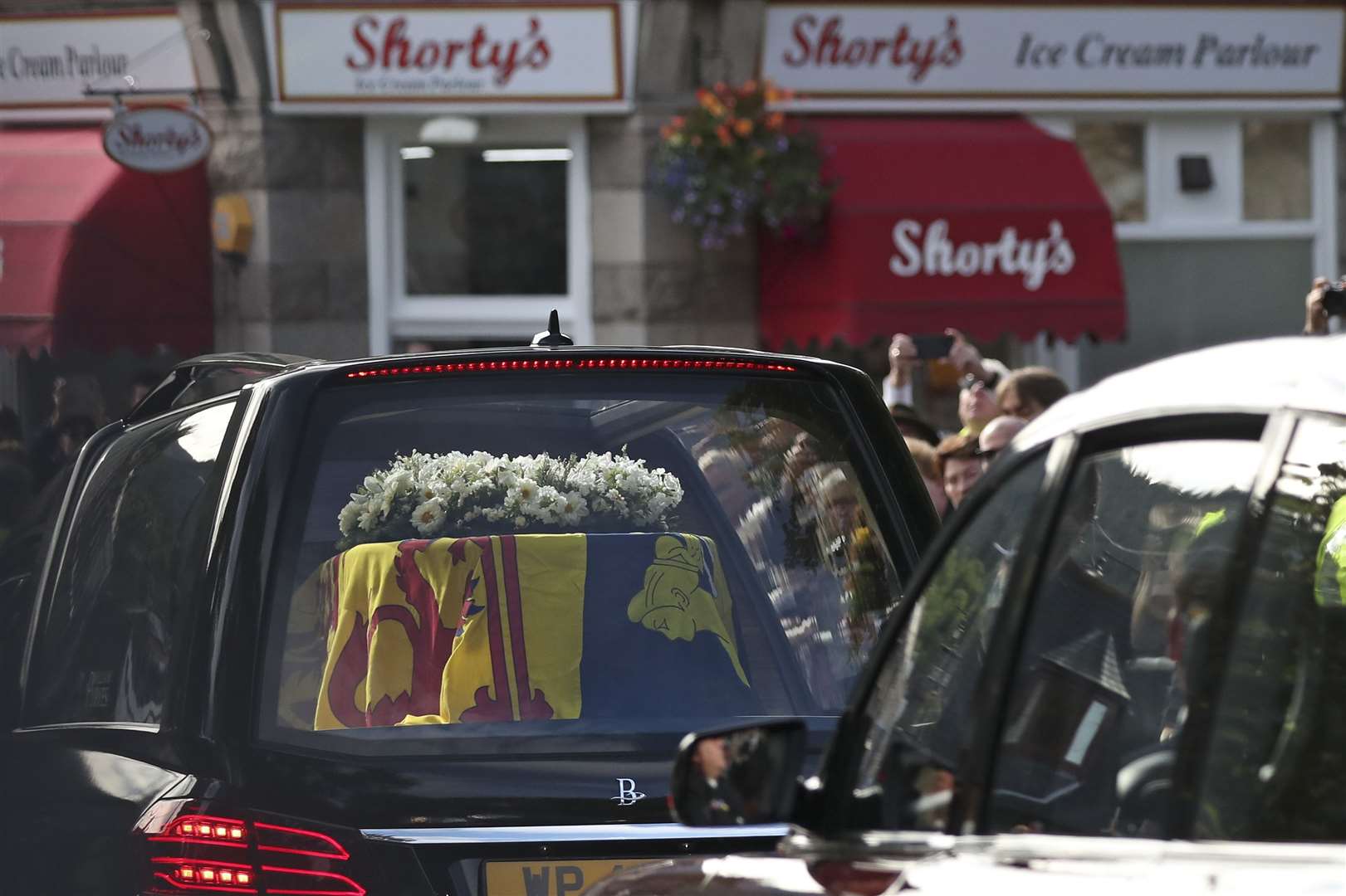 Members of the public line the streets in Ballater, Scotland, as the hearse carrying the coffin of Queen Elizabeth II passes through (Scott Heppell/AP)