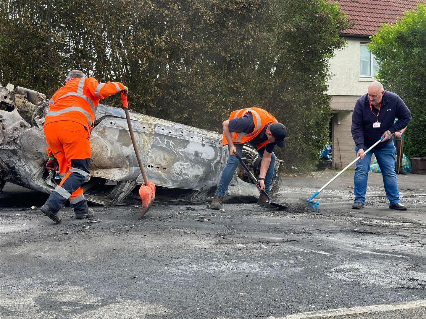 Council workers clear debris from the area immediately around a car that was set alight in Ely, Cardiff (PA)