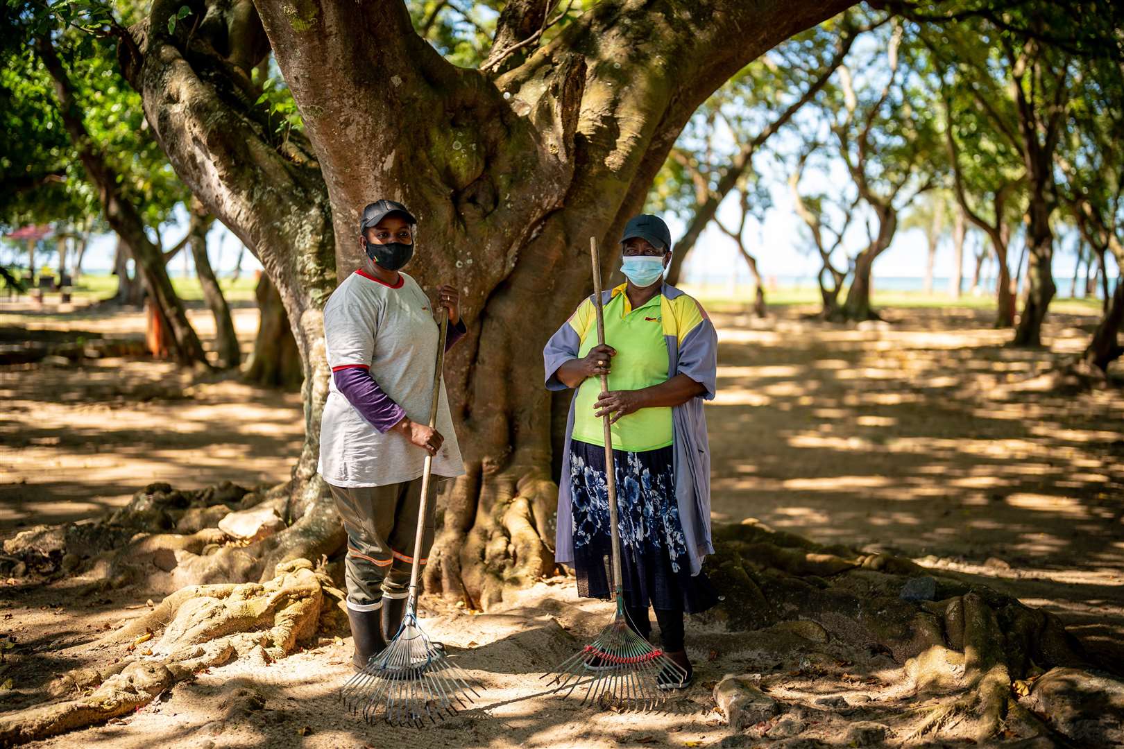 Cleaners wear face masks, in accordance with government guidelines, as they take a break under a tree while clearing litter in a park in Mauritius (Ben Birchall/PA)