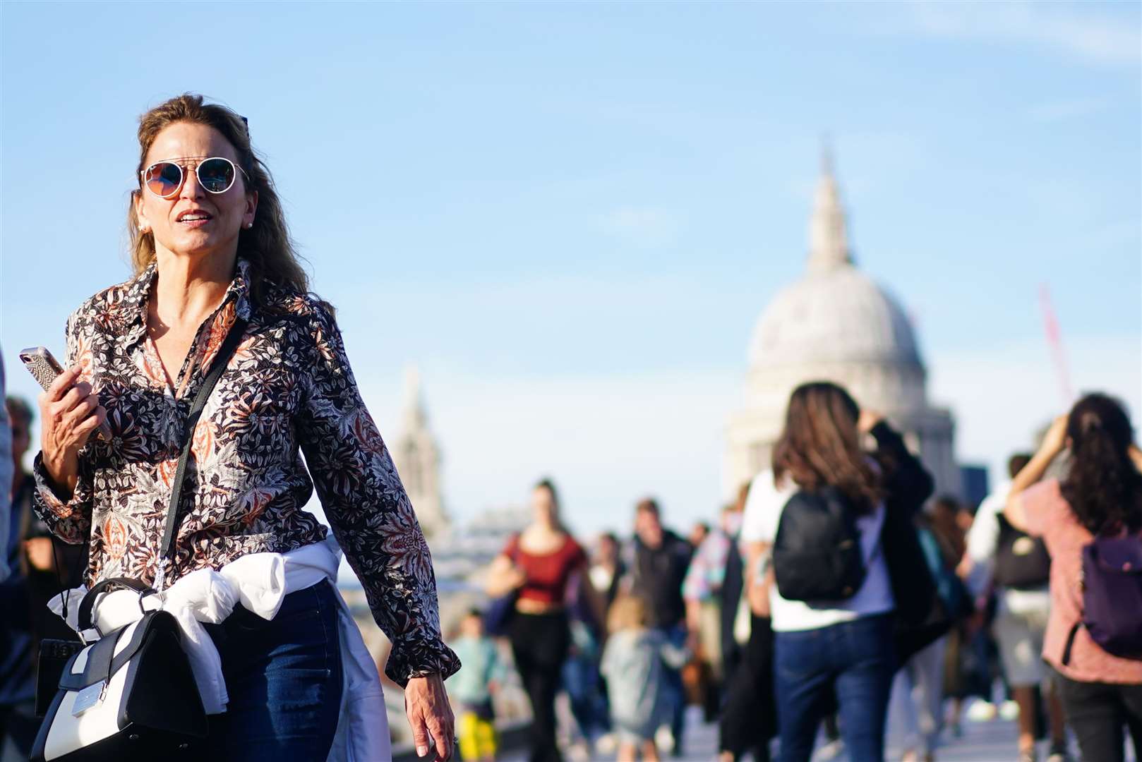 People enjoy the sunshine as they walk across Millennium Bridge in London (Victoria Jones/PA)