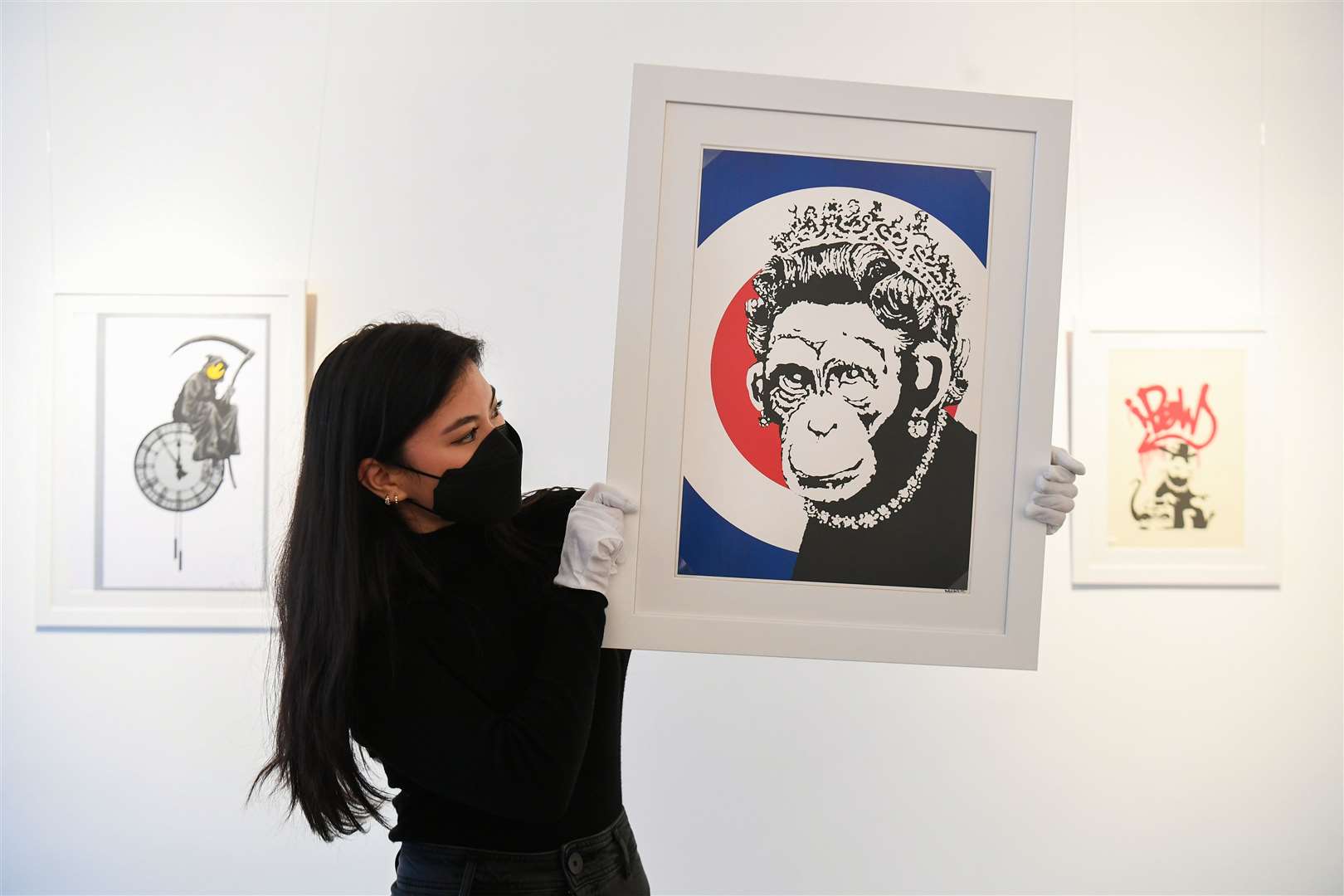 Gallery assistant Sophia Shim holds a limited edition print of Monkey Queen (2003) by Banksy (Kirsty O’Connor/PA)