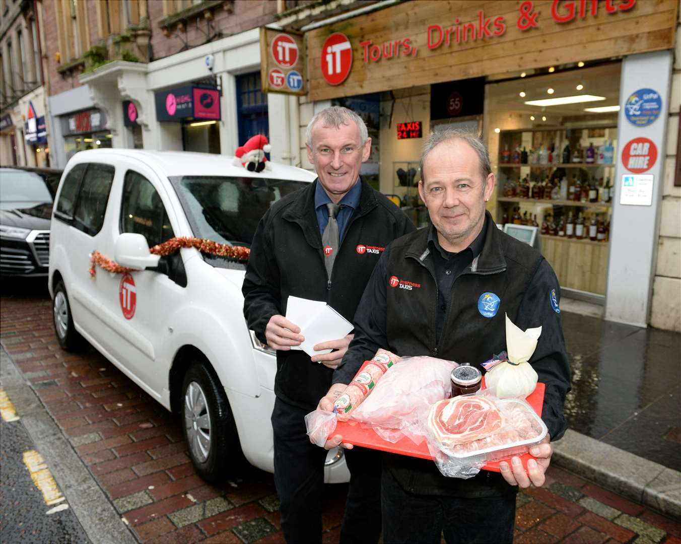 Inverness Taxis are offering a car, panto tickets and a turkey hamper to a family in need..Gavin Johnston, Inverness Taxis Director and Dougie Bolt, stand outside the Inverness Taxis headquarters holding the panto tickets and Christmas hamper infront of the car that are all being given away to a family in need..Picture: James MacKenzie..