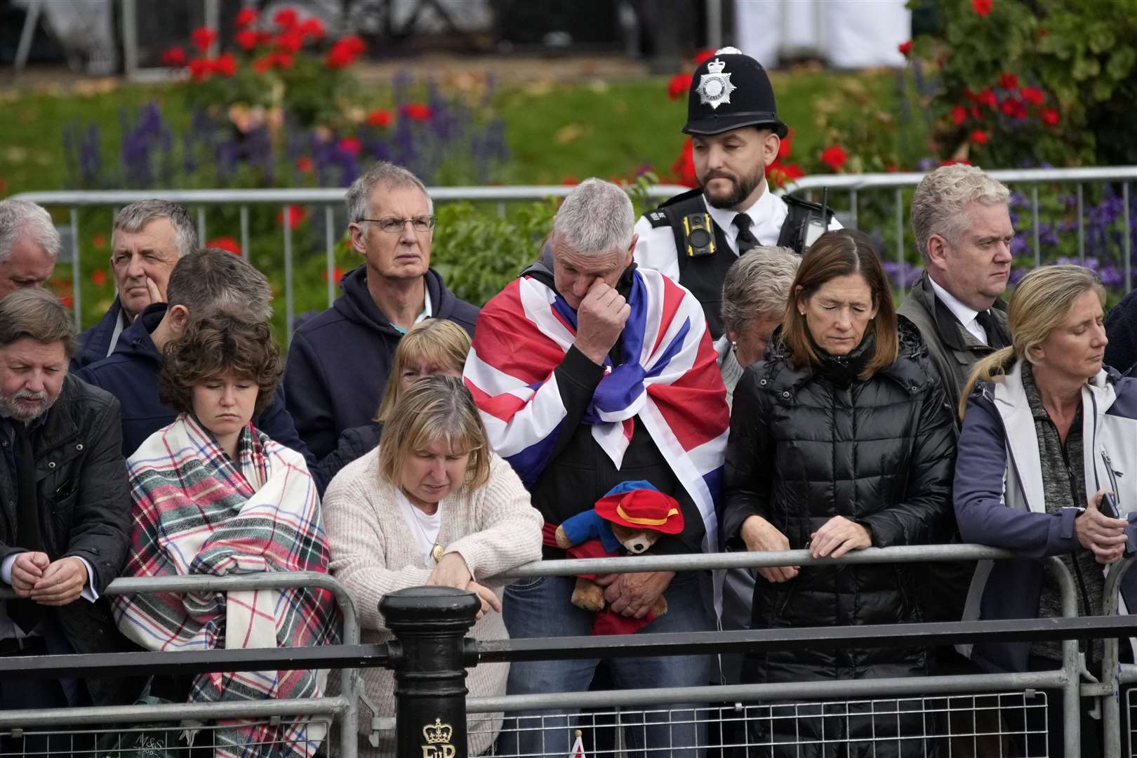 Members of the public, one of them holding a Paddington Bear toy, outside Buckingham Palace watching the funeral procession (Christophe Ena/PA)