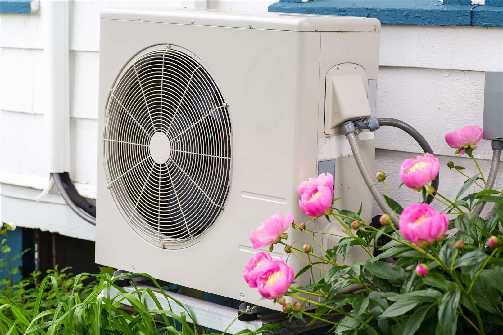 Air conditioning/ Heat pump unit on the side of a home among the flowers..