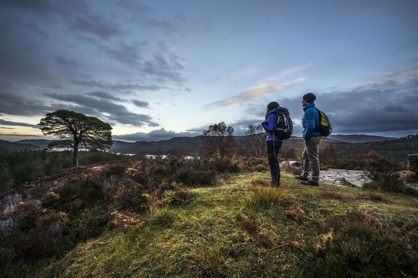 Walking in the Glen Affric area, a couple of walkers standing looking over the landscape of the national nature reserve, river and moorland.