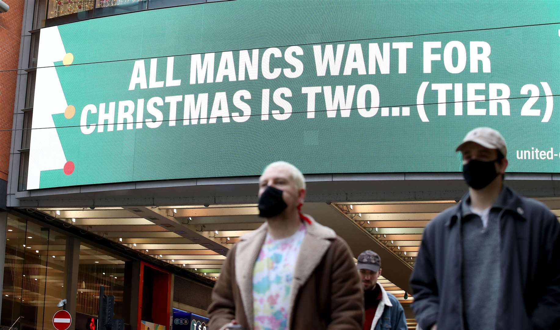 People wearing face masks walk past a sign on Market Street, Manchester (Martin Rickett/PA)