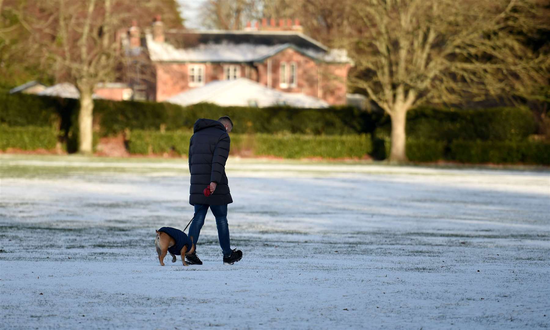 Dog walker going through light snow in Bught Park.