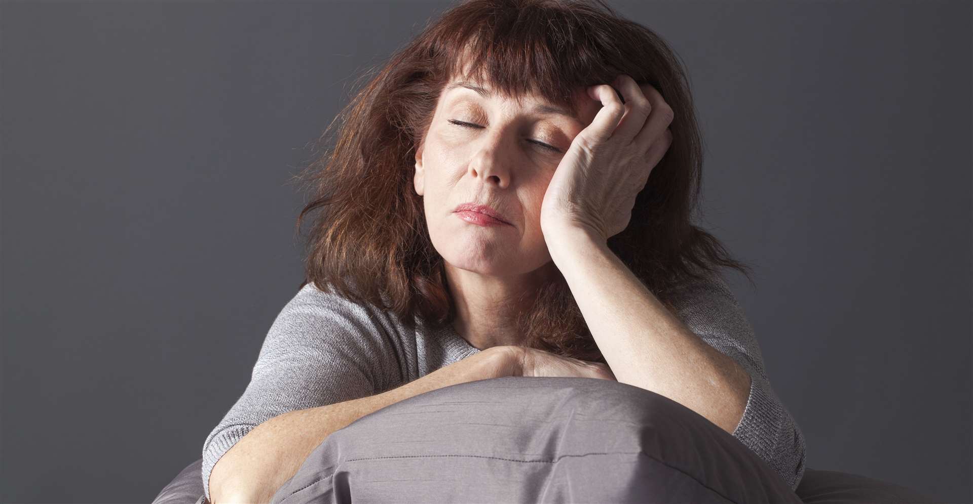 exhausted mature woman resting her face and hands laying down on cushions for comfort while being sick or depressed.