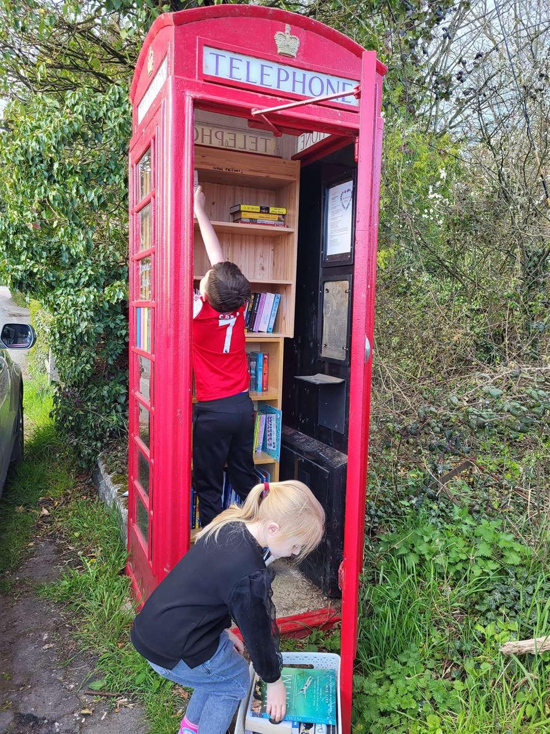 Ms Connolly’s two younger children helping to add books to shelves in the telephone box library (Iona Connolly/PA)
