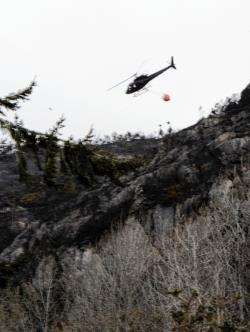 A helicopter waterbombs the blackened hillside at Aigas
