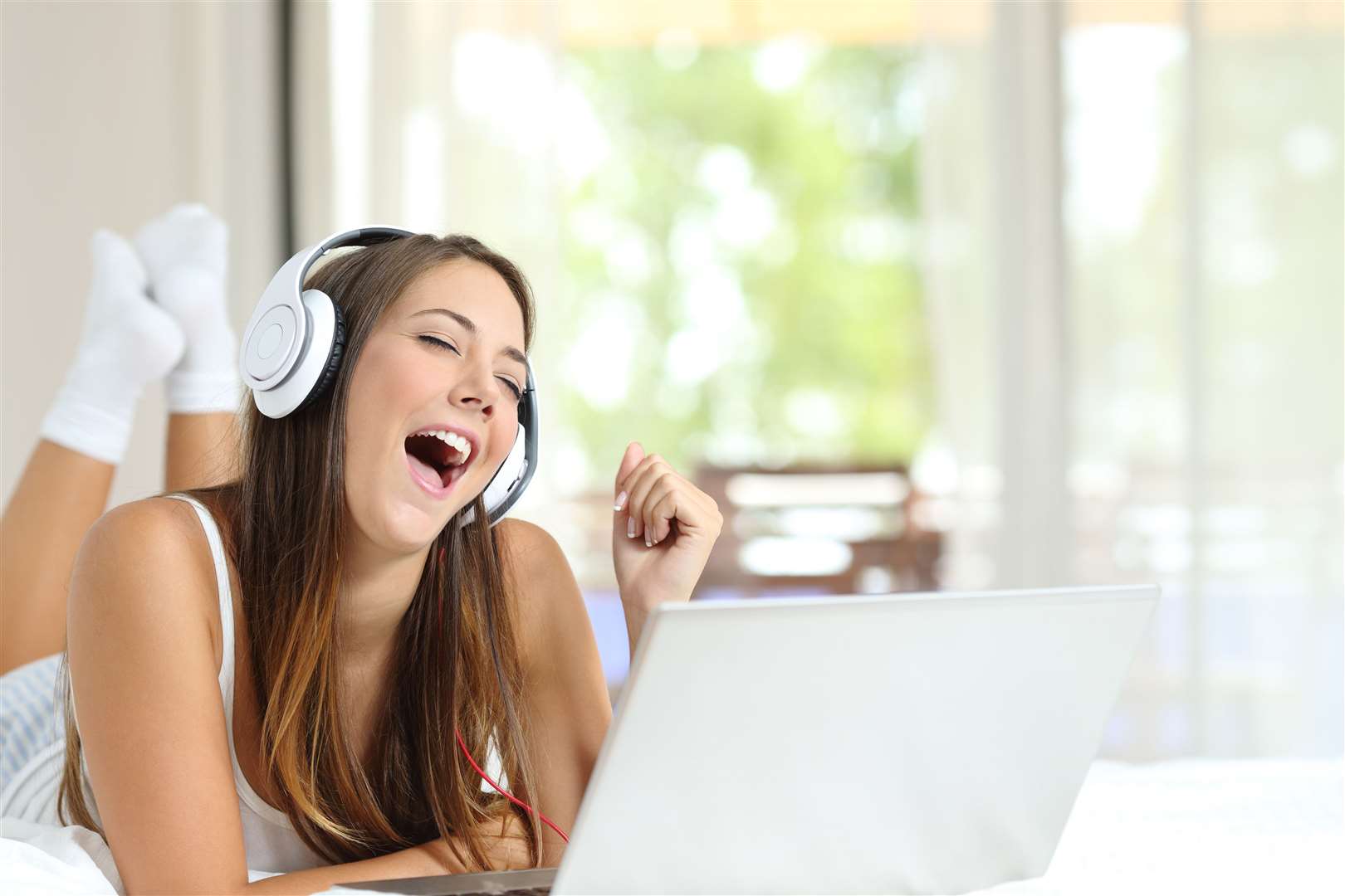 Girl with headphones singing listening music on laptop