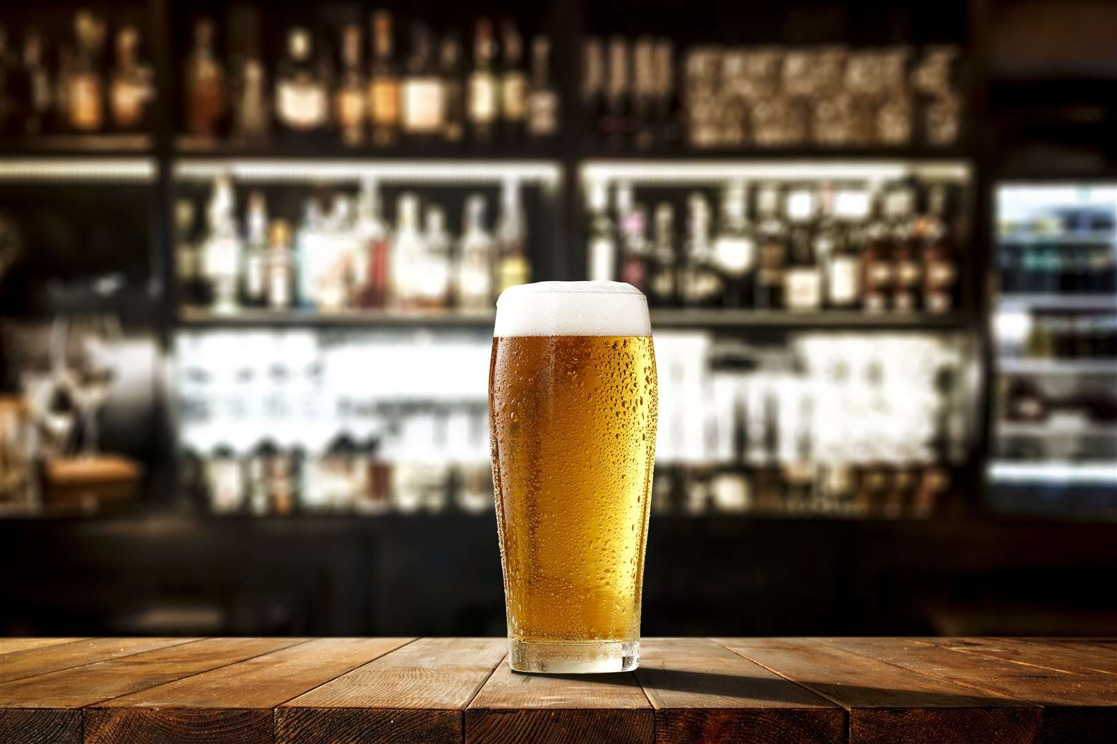 Glass of beer on wooden board and blurred bar background.