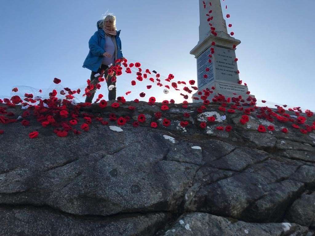 Mrs Lyn Woods helps to position the poppy netting at Stratherrick War Memorial