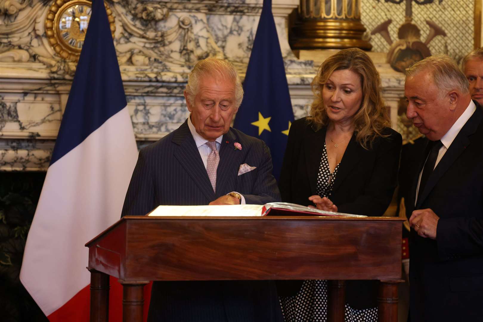 The King, watched by the President of the Senate, Mr Gerard Larcher, and the President of the National Assembly, Mrs Yael Braun-Pivet, signing the visitors book (Ian Vogler/Daily Mirror/PA)