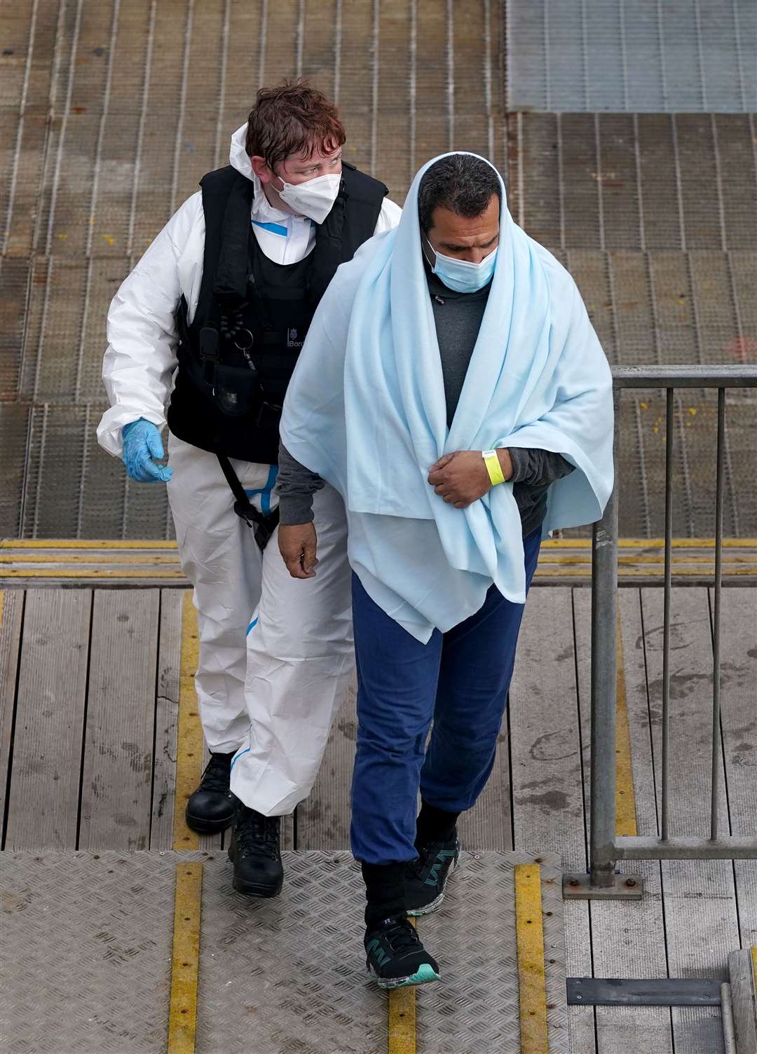 A man is seen exiting the jetty covered in a blanket after being removed from one of the boats (Gareth Fuller/PA)