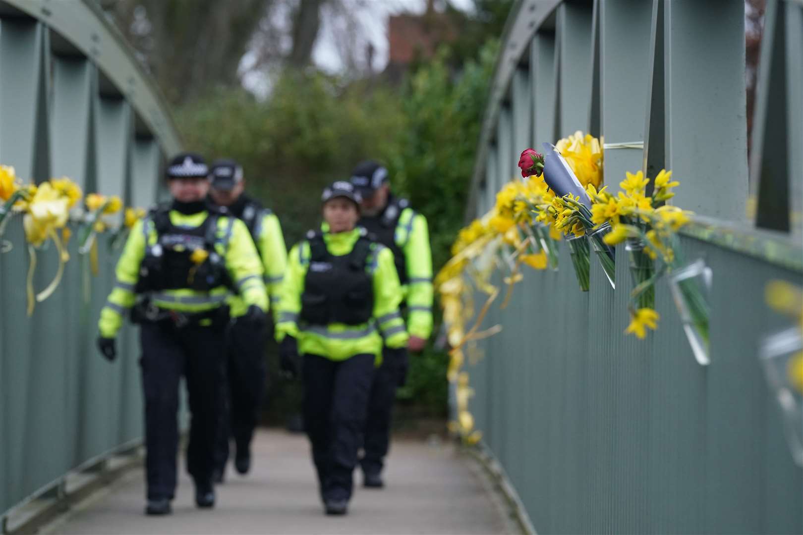 Police officers walk past flowers and yellow ribbons tied to a bridge for Nicola Bulley over the River Wyre (Owen Humphreys/PA)