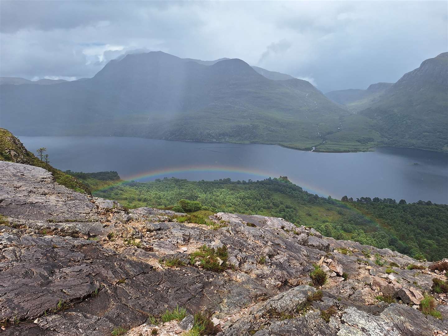 A rainbow appears over the woodland below, with Slioch in the background.