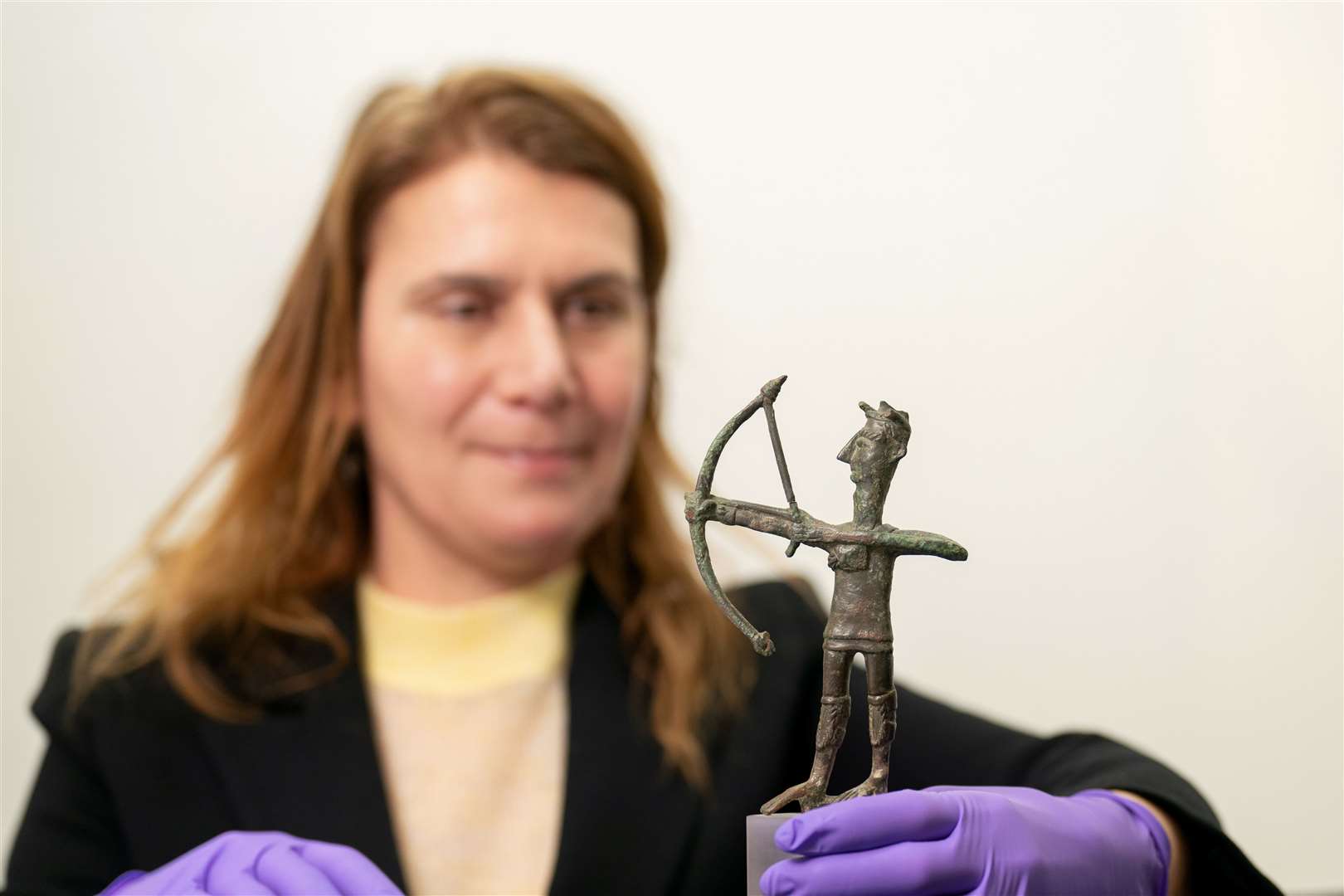 Exhibition curator Dr Anastasia Christophilopoulou inspects a bronze figurine of an archer (Joe Giddens/PA)
