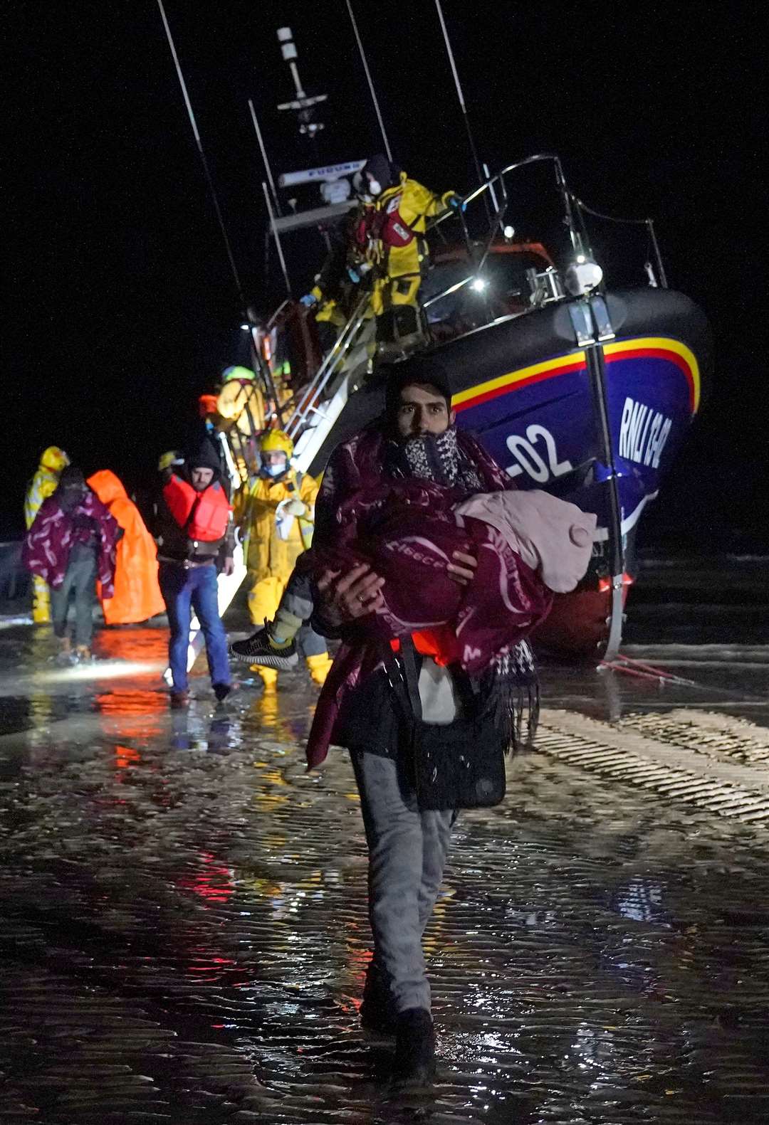 (PA/ Gareth Fuller) A man carries a baby as a group of people thought to be migrants are brought in to Dungeness, Kent, after being rescued by the RNLI