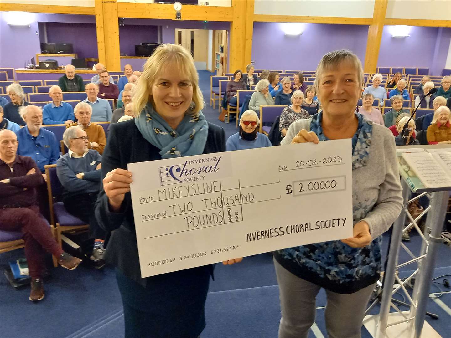 Emily Stokes, CEO of charity Mikeysline receives the cheque from Andrea Gritter one of the carolthon organisers as Inverness Choral Society's members look on.