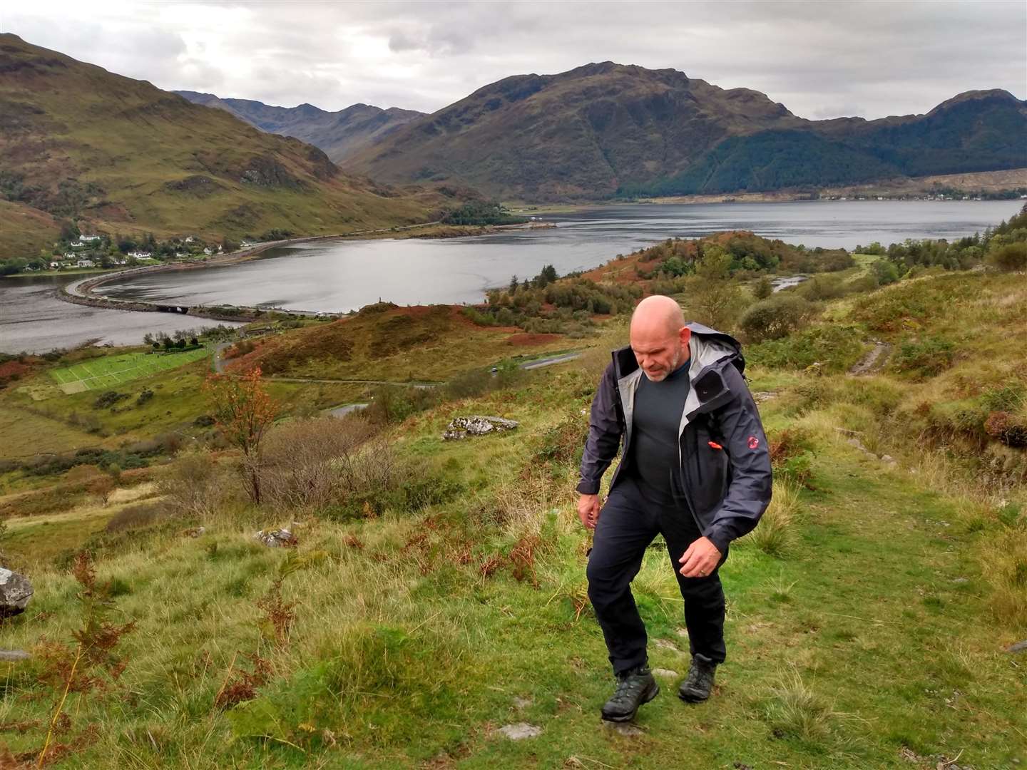 Eric climbs up the path with Loch Duich and the causeway behind.