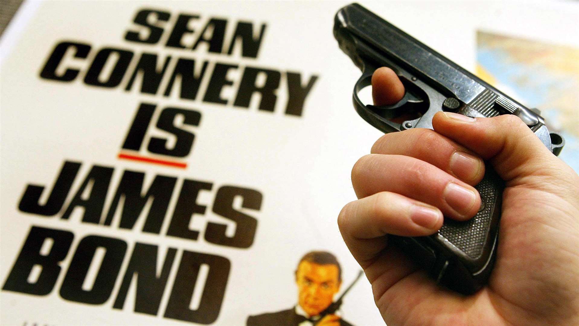 A Walther PPK handgun in front of a James Bond poster (PA)