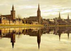 The spires of Inverness churches reflected in a calm River Ness.