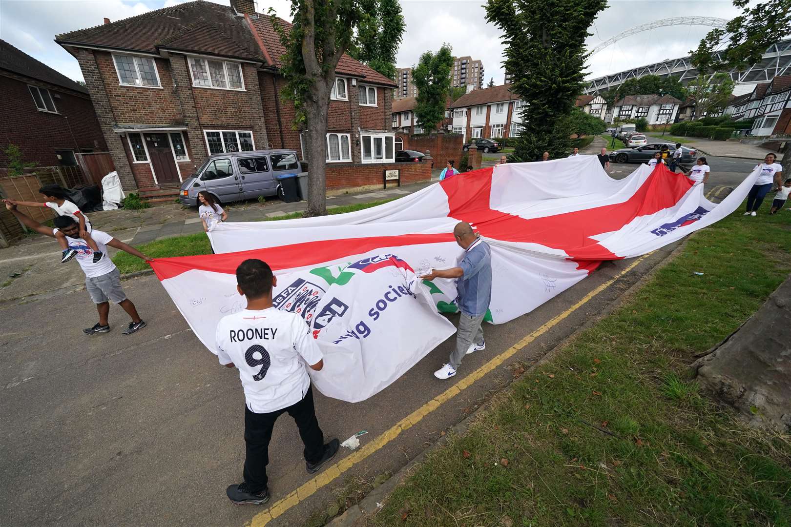 Local residents carry an official giant England Nationwide respect campaign flag from Neeld Crescent in Brent, where Raheem Sterling grew up, to Wembley Stadium, ahead of the Euro 2020 final (Jonathan Brady/PA)