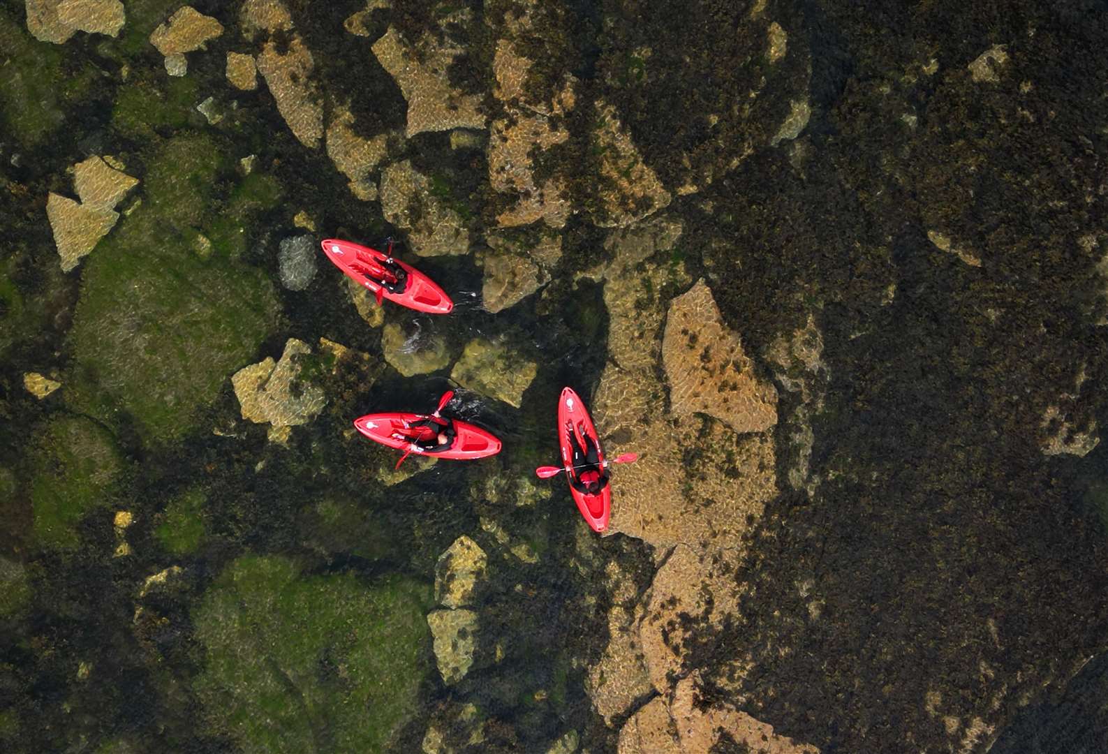 Kayakers seen from above skim over the clear water of the bay (Owen Humphries/PA)